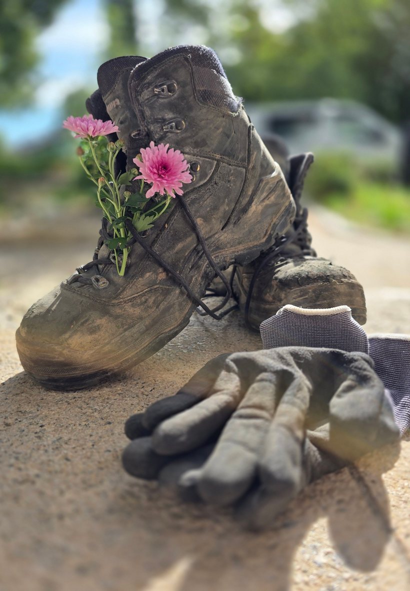 Arbeitsschuhe mit Blumen im Schnürsenkel und Arbeitshandschuhe nach getaner Arbeit